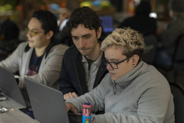três pessoas sentadas em frente a um computador aprendendo