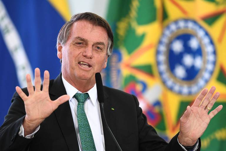 Bolsonaro gesticula enquanto fala. Ao fundo podem ser vistas bandeiras do Brasil.