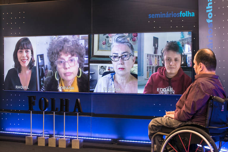 Na foto, Jairo Marques aparece sentado em uma cadeira de rodas, no canto direito. Do lado dele, um telão tem as imagens dos convidados e da mediadora. Na frente, letras formam a palavra "Folha".