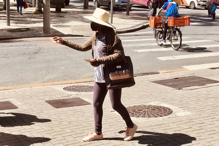 Graziela Pereira, 60, de chapéu e bolsa, distribui panfletos no centro de Curitiba 