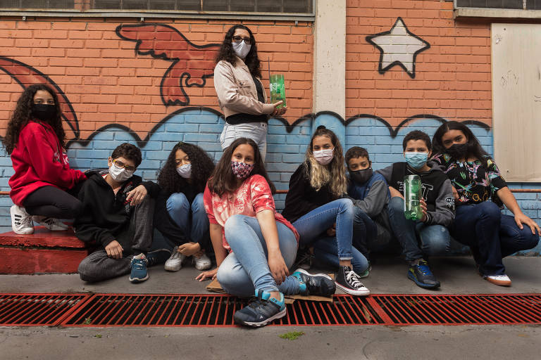 Mulher com máscara segura garrafa PET verde com uma régua usada para medir chuvas; ela está rodeada por oito adolescentes, que estão sentados