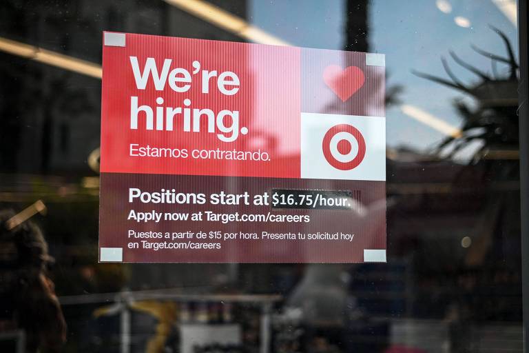 Um anúncio em vermelho fixado em vidro de loja diz: "estamos contratando"