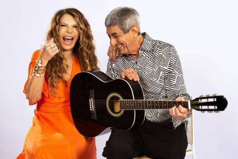 Em foto colorida a cantora Elba Ramalho e o cantor Raimundo Fagner, empunhando um violão, sorriem