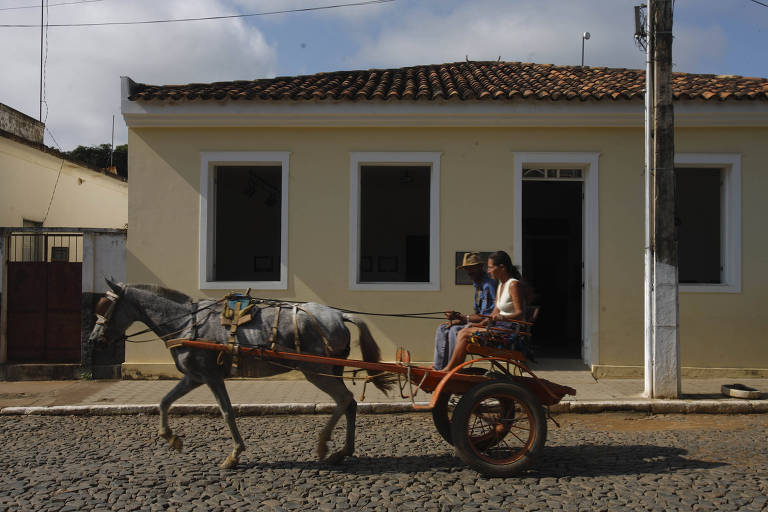 Cassal em charrete passa em frente a uma casa amarela em que funciona o memorial do sambista Ataulfo Alves em Miraí (MG)