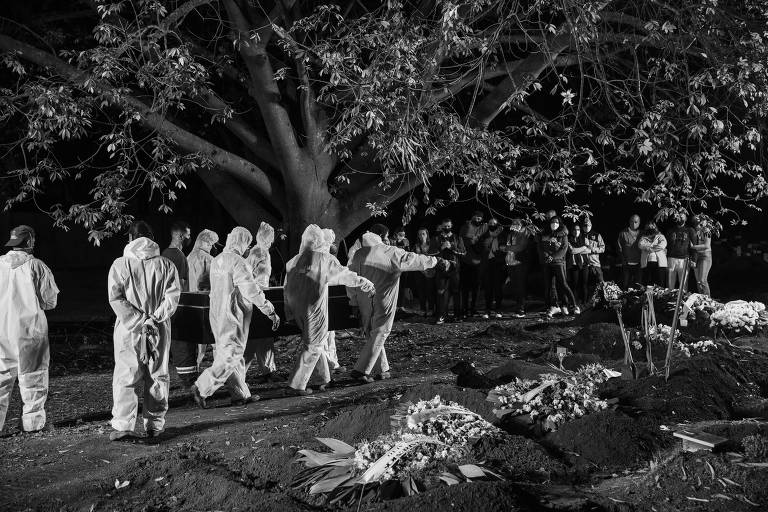 Grupo de sepultadores com roupas brancas de proteção carregam caixão em direção a uma cova aberta