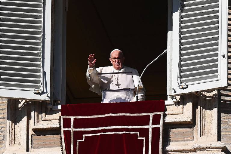 Vestido de branco, papa acena a fiéis dentro de um edifício, por meio de uma grande janela 