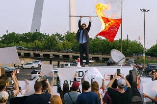 Peter McIndoe, the 23-year-old creator of the Birds Aren't Real movement, burns a Cardinals flag in St. Louis during a satirical protest of the baseball teamÕs logo in July 2021.   (Madeline Houston via The New York Times)