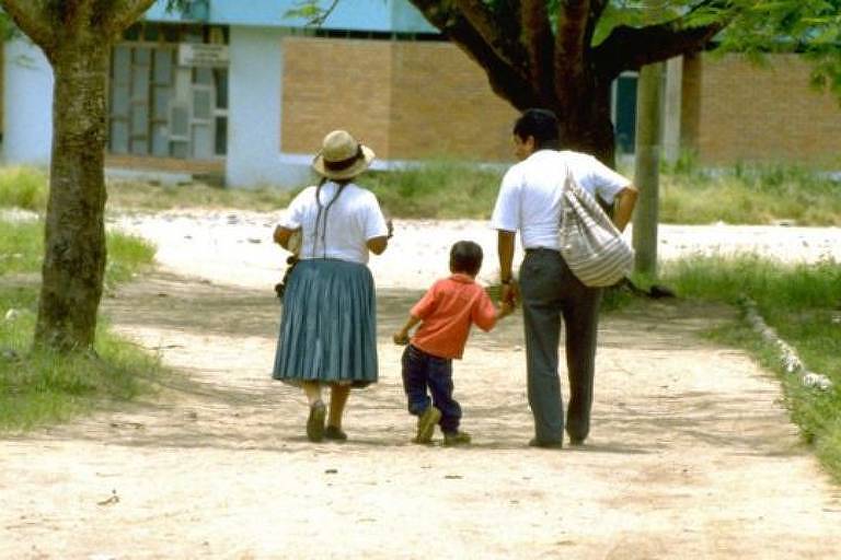 De costas, uma mulher, uma criança e um homem caminham sobre uma estrada de terra
