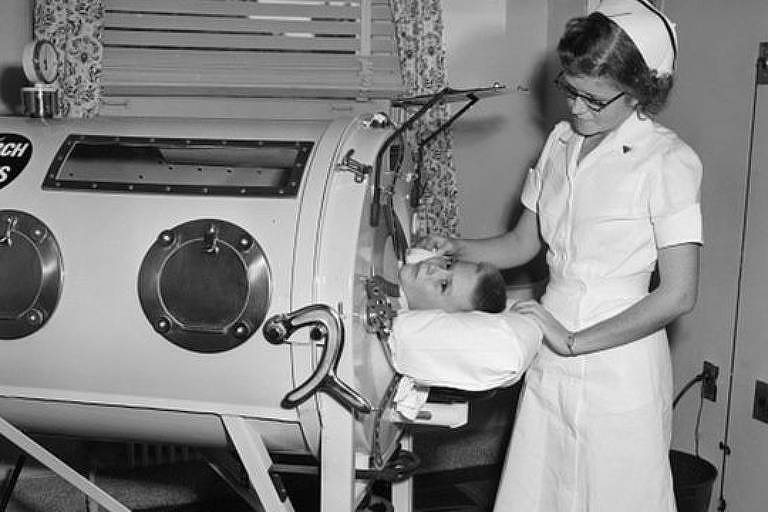 Imagem em preto e branco mostra uma criança deitada em um aparelho e uma enfermeira ao seu lado
