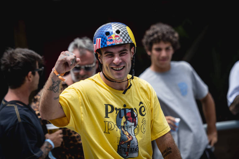 Pedro Barros de camiseta amarela e capacete azul e cinza, comemorando com o punho direito erguido