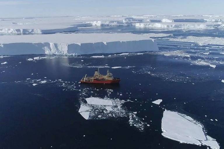 Imagem aérea mostra navio no meio de um mar gelado. Ao fundo, se vê geleiras.