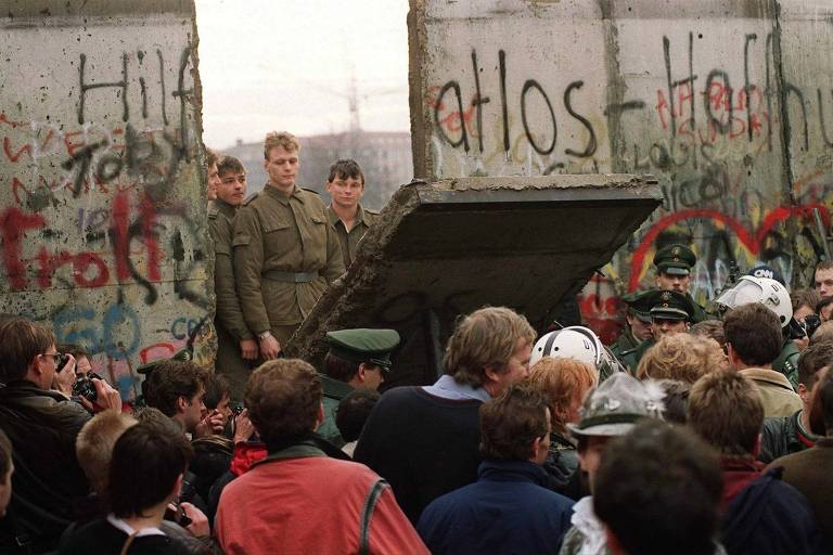 Berlinenses ocidentais se aglomeram em frente ao Muro de Berlim, enquanto assistem aos guardas da fronteira da Alemanha Oriental demolirem um trecho do muro, perto da Praça Potsdamer
