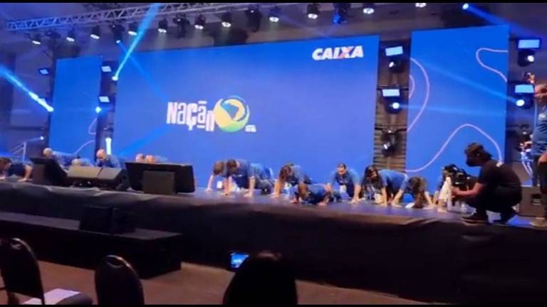 Pessoas fazendo flexões em palco, com tela azul ao fundo 