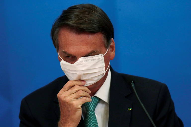 Bolsonaro está com a mão direita na região da boca, tentando ajustar a máscara de proteção contra Covid