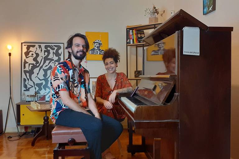 Em foto colorida e sentados diante de um piano de armário estão o pianista Salomão Soares e a cantora Vanessa Moreno sorrindo