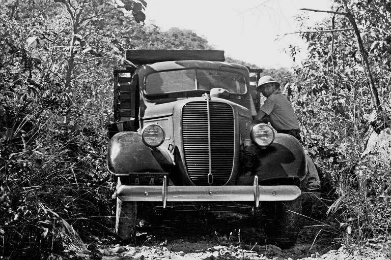 Retrato em preto e branco de homem em cima de caminhonete atolada em meio a mata 