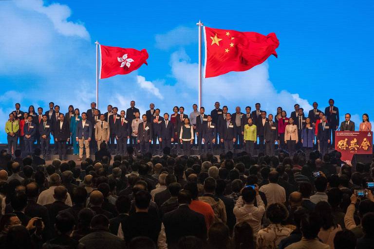 Candidatos ao Conselho Legislativo cantam o hino chinês em fórum eleitoral; bandeira da China está em primeiro plano, e a de Hong Kong, em segundo