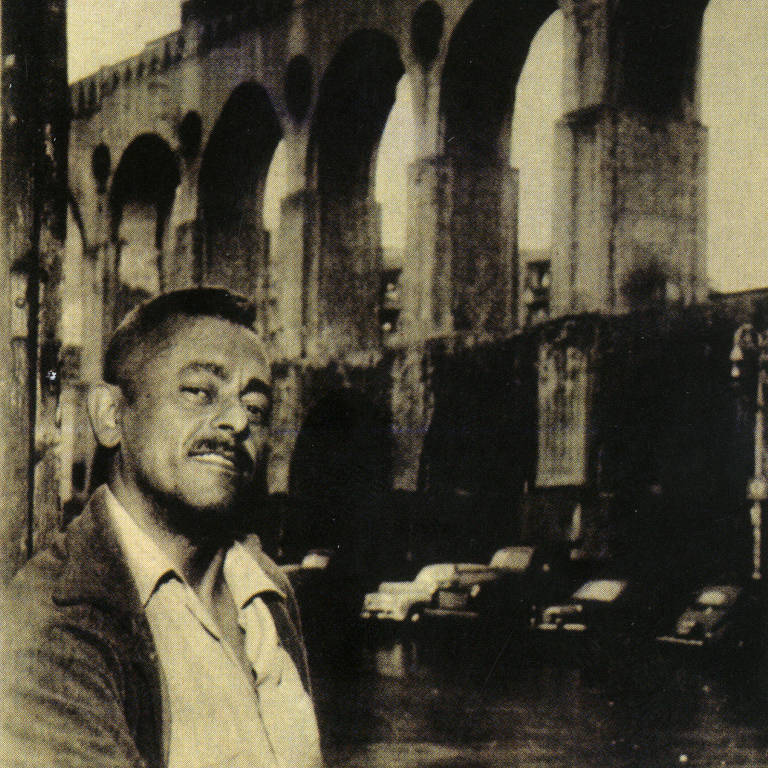 O compositor Assis Valente em 1951, diante de painel fotográfico que reproduz os arcos da Lapa, em imagem da biografia 'Quem Samba Tem Alegria'