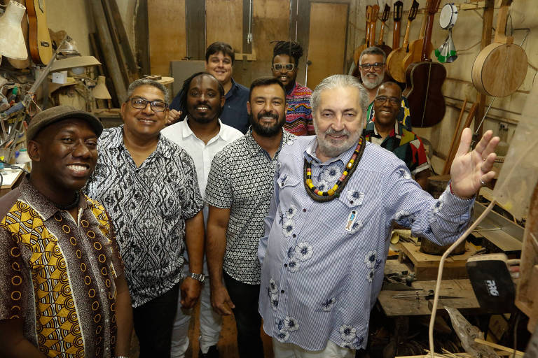 Em foto colorida os oito integrantes do grupo Samba do Trabalhador posam para a câmera com o sambista Moacyr Luz, que está com a mão esquerda levantada