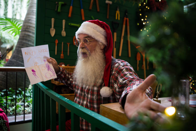 Um Papai Noel aparece de braços abertos, conversando com o público do shopping