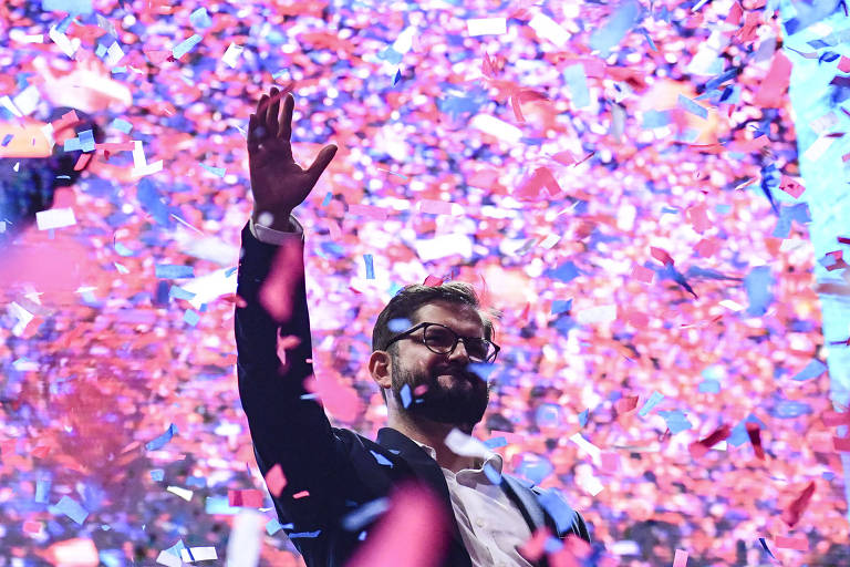 Homem de terno e óculos com mão levantada em meio a confetes coloridos