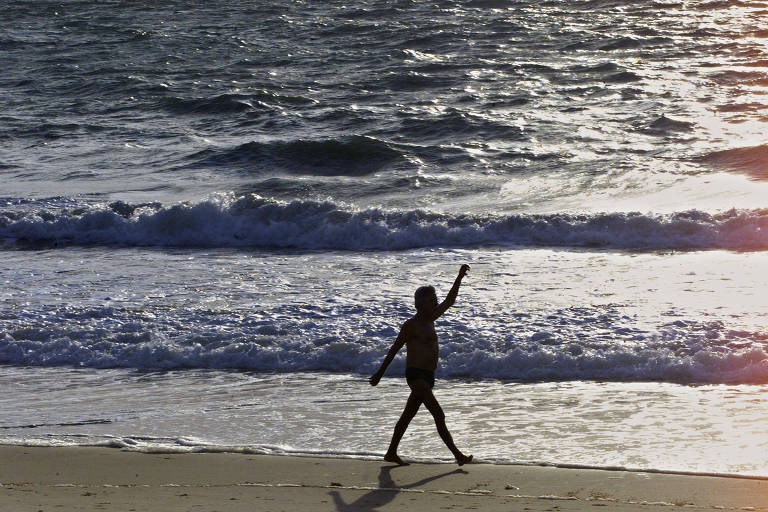 homem caminha erguendo os braços a beira do mar 