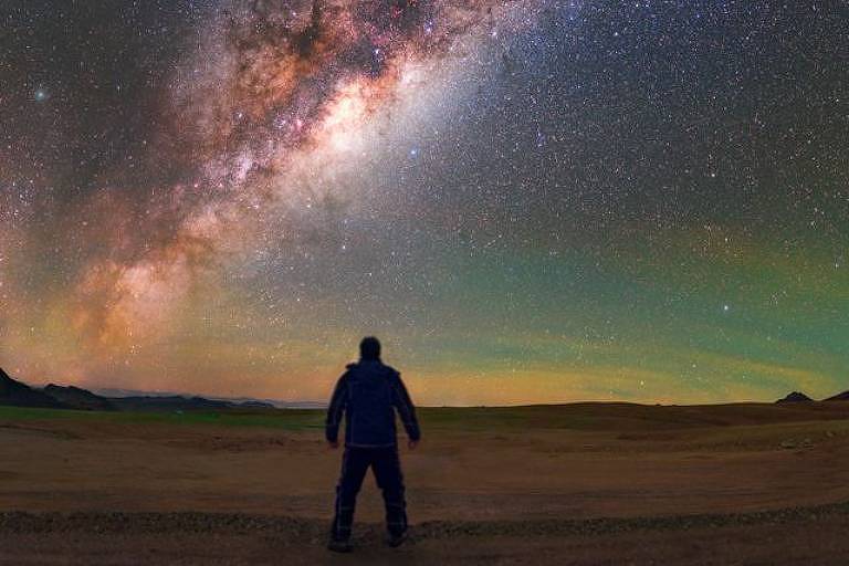 Imagem em primeiro plano mostra homem de costas olhando para um céu estrelado