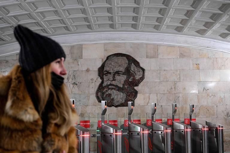 Mulher com máscara em frente a imagem de Karl Marx no metrô de Moscou, na Rússia