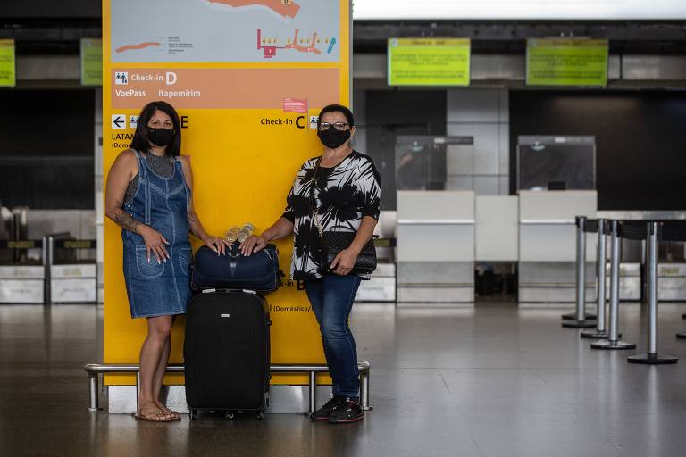 Duas mulheres aguardam com malas em frente a um guichê