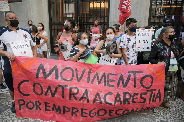 Grupo de pessoas carregam uma faixa grande e cartazes durante protesto na frente da Bolsa de Valores de São Paulo 