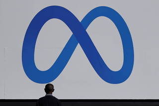 FILE PHOTO: A man stands in front of a sign of Meta, the new name for the company formerly known as Facebook, at its headquarters in Menlo Park