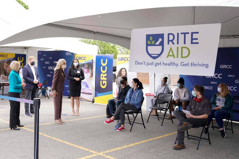 Pessoas em pé, em toldo branco, ao lado de placa onde está escrito "Rite Aid"