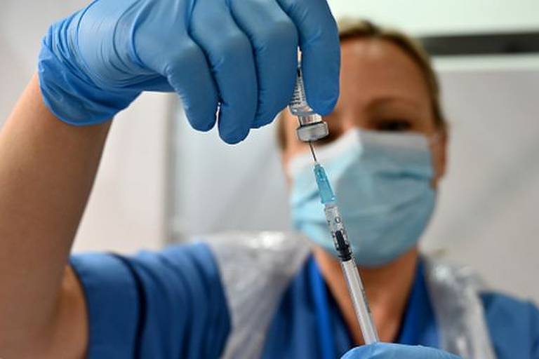 Imagem em close mostra profissional da saúde de máscara espetando uma seringa em uma ampola de vacina