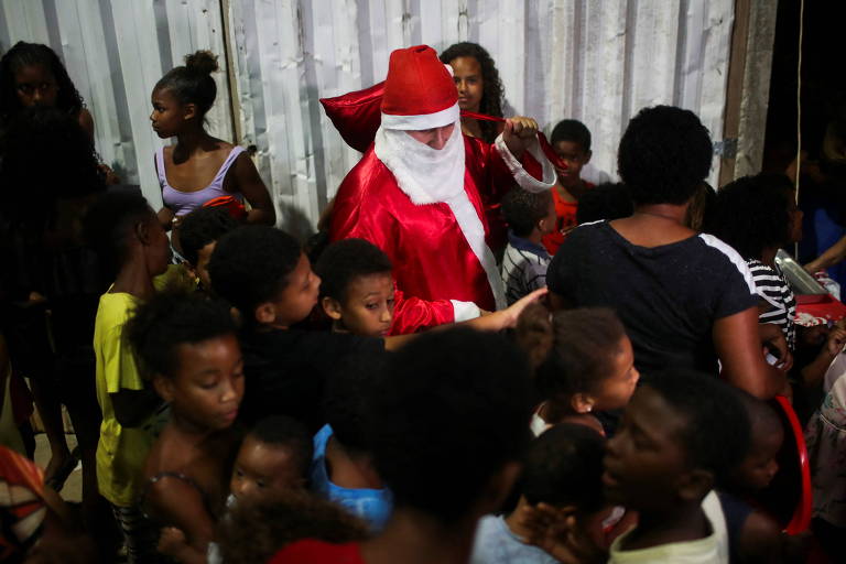 Homem vestido de Papai Noel é cercado por crianças antes de distribuir brinquedos que foram doados para festa de Natal na Cidade de Deus, no Rio de Janeiro