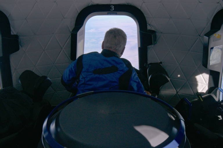 William Shatner olha pela janela de uma cápsula, vendo a Terra do alto, no espaço