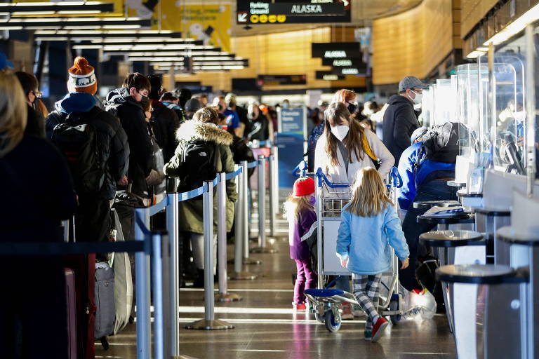 Pessoas aguardam em fila de checkin de aeroporto nos estados unidos; à direita, mulher empurra carrinho que tem duas crianças em cima 