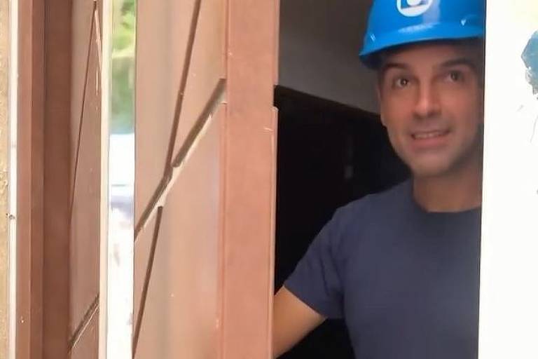 Homem abrindo porta usando capacete azul claro e camiseta azul escura