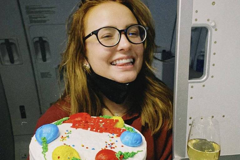 Mulher branca com cabelo liso usando óculos segurando bolo de aniversário