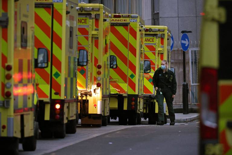 Fila de ambulâncias; na última, ao fundo da foto, uma profissional de saúde se apoia sobre o carro