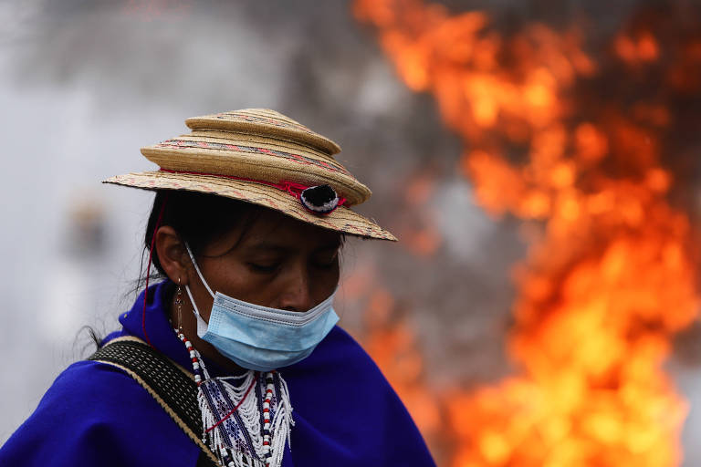 Integrante de comunidade indígena durante os protestos que marcaram a greve geral em Bogotá, ao fundo, uma labareda de fogo