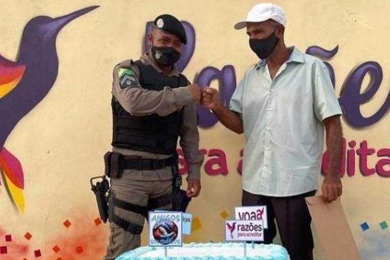 Policial cumprimentando homem em frente a um bolo enfeitado