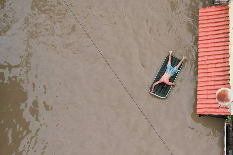 Homem usa um colchão inflável para se locomover em rua alagada pelo rio Cachoeira na cidade de Itabuna, no sul da Bahia, região que está sendo castigada pelas enchentes neste final de 2021