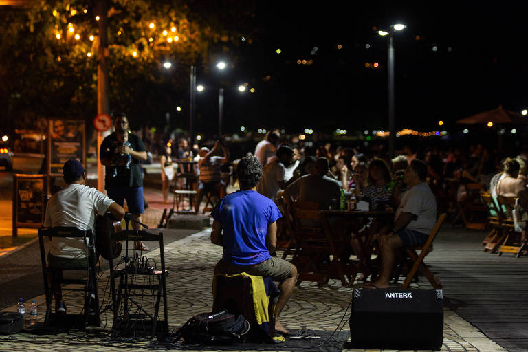 Pessoas sentadas em praça assistindo a uma apresentação musical