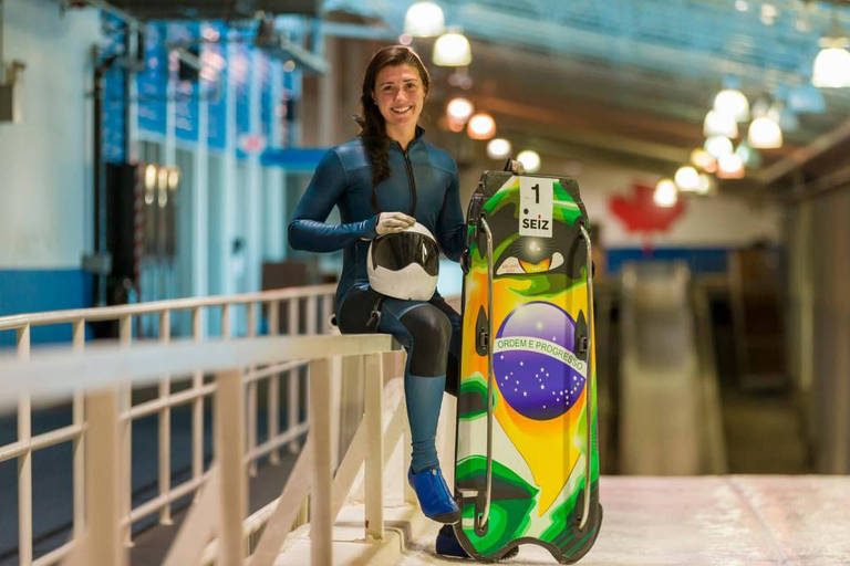 Nicole posa ao lado do trenó pintado com a bandeira do Brasil, segurando o capacete na mão