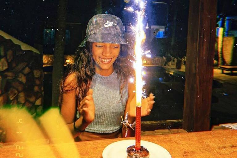 Rayssa Leal, uma adolescente negra, sorri em frente a um bolo com vela acesa em sua festa de aniversário de 14 anos