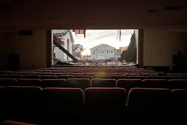 Foto mostra uma sala de cinema, onde há várias cadeiras. No lugar onde fica a tela, há um buraco, por onde é possível ver o lado de fora.
