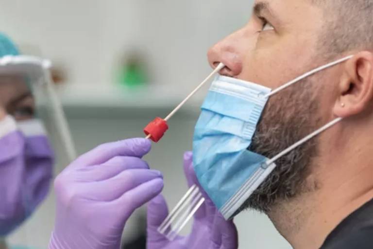 Imagemem close mostra profissional da saúde fazendo um teste de Covid em um homem colocando uma haste flexível no nariz dele