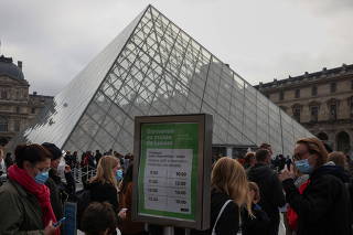 People wearing facemasks queue to enter the Louvre in Paris