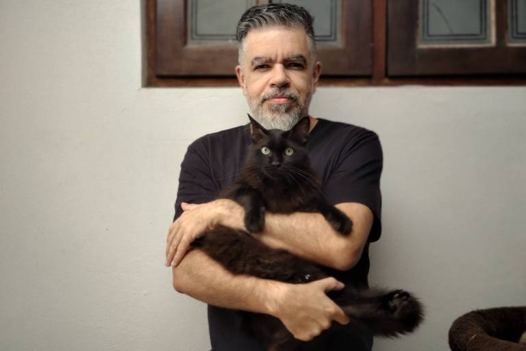 Cristiano Cunha, fundador da Allegro Cat Sitters, abraça um gato preto
