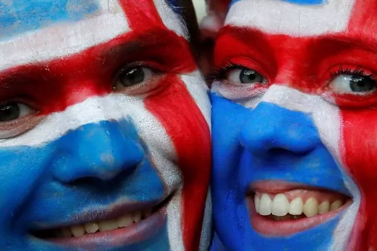 Homem e mulher sorrindo com os rostos pintados com a cor da bandeira da Islândia (branco, vermelho e azul)